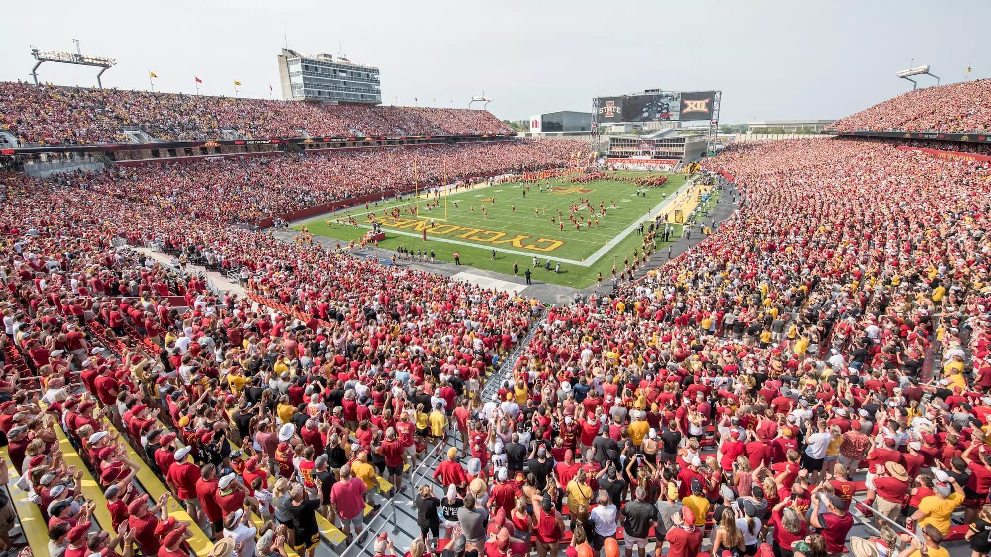 Jack Trice Stadium at capacity — cardinal and gold to the rim, CYCLONES painted across the end zone as the band takes the field