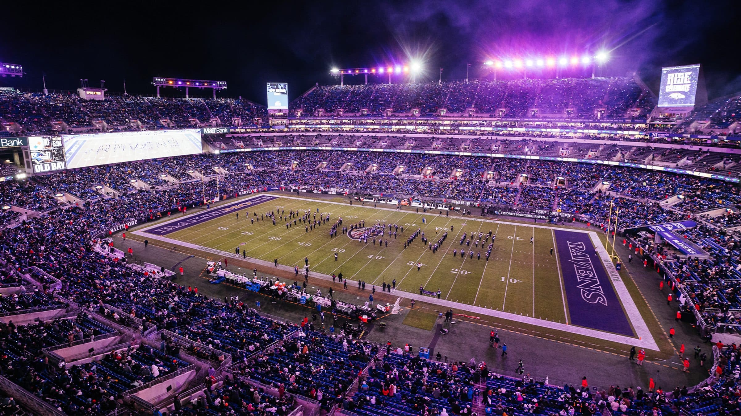 A general view of M&T Bank Stadium packed with purple-clad Baltimore Ravens fans on game day, the downtown skyline visible beyond the upper deck