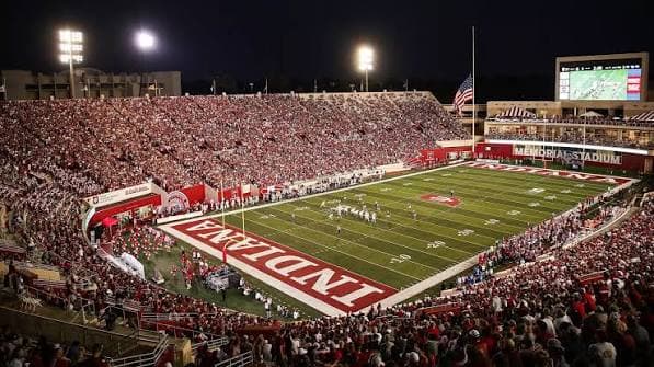 Memorial Stadium under the lights — a crimson-and-cream crowd filling The Rock with the INDIANA end zone in the near corner
