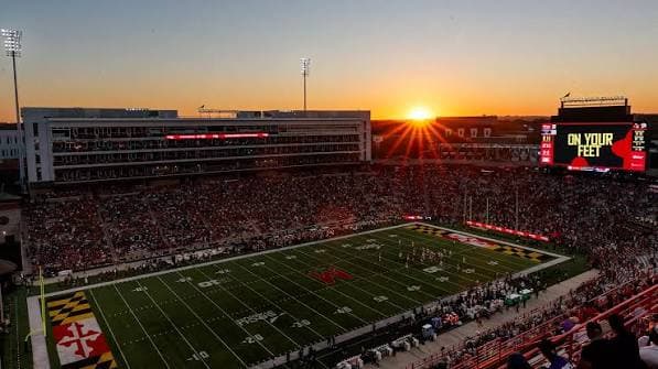 Sunset over SECU Stadium — the Maryland flag pattern painted in both end zones as the videoboard glows above the stands