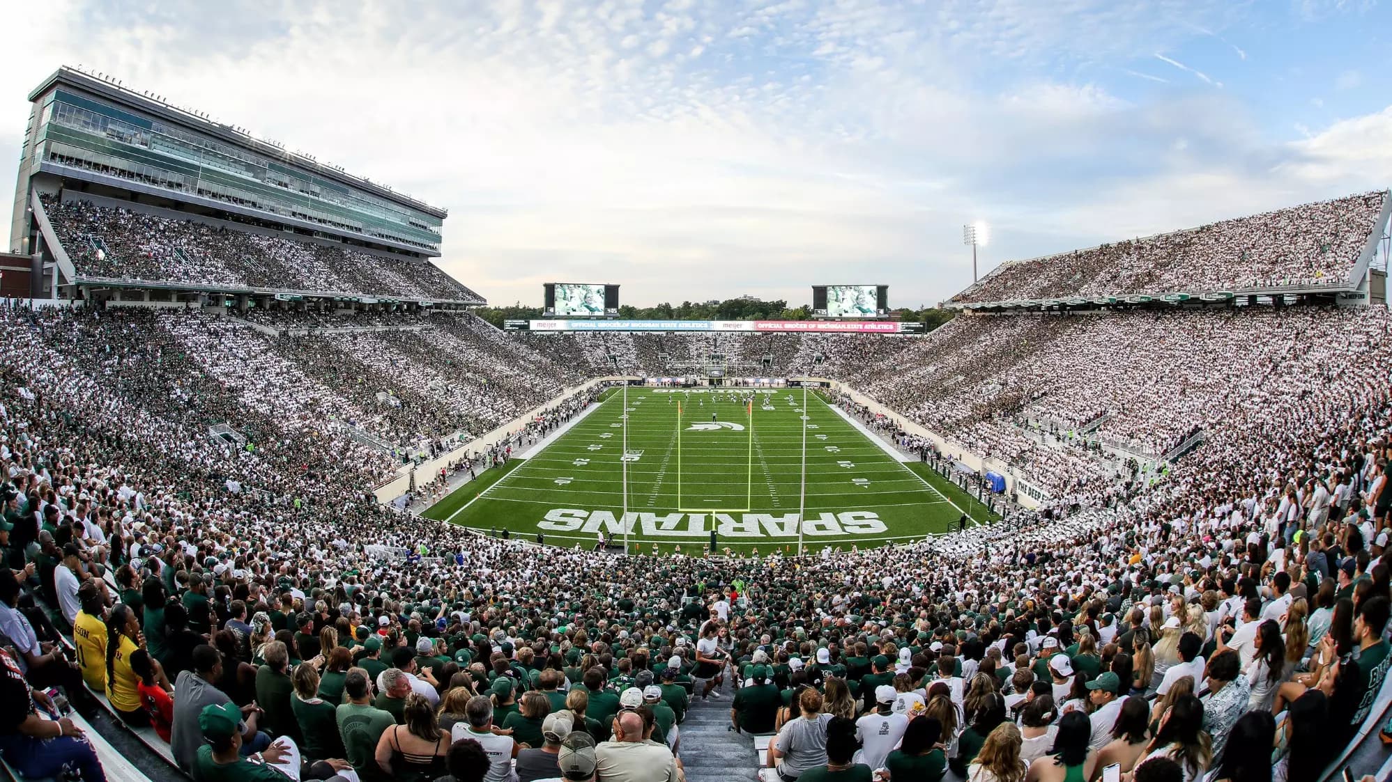 Spartan Stadium during a white-out — a full house in white and green with the SPARTANS end zone and Spartan helmet logo at midfield