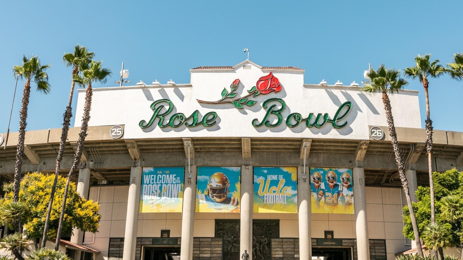 The Rose Bowl's famous entrance — the rose-topped neon sign over the main gate, framed by palm trees and UCLA football banners