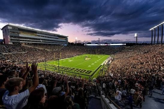 Ross-Ade Stadium at dusk — a packed house under dramatic storm-lit clouds with the BOILERMAKERS end zone below