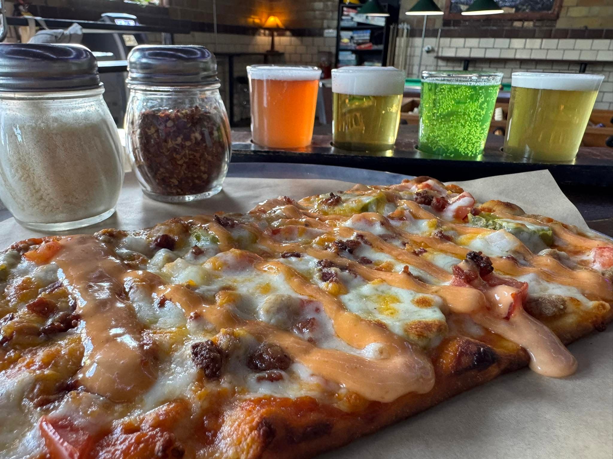 A flatbread pizza with pepper jelly and jalapeños at Torrent Brewing, a flight of four beers lined up beside it