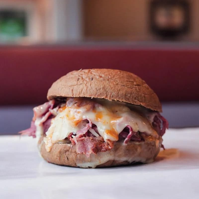 A stacked corned beef Reuben sandwich with melted cheese on a toasted seeded bun at West Street Deli
