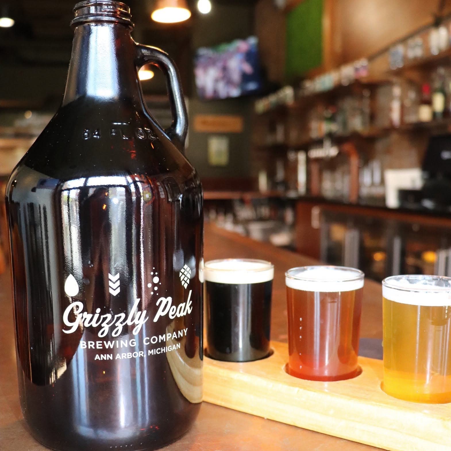 A Grizzly Peak Brewing Company growler beside a flight of four house-brewed beers on the bar