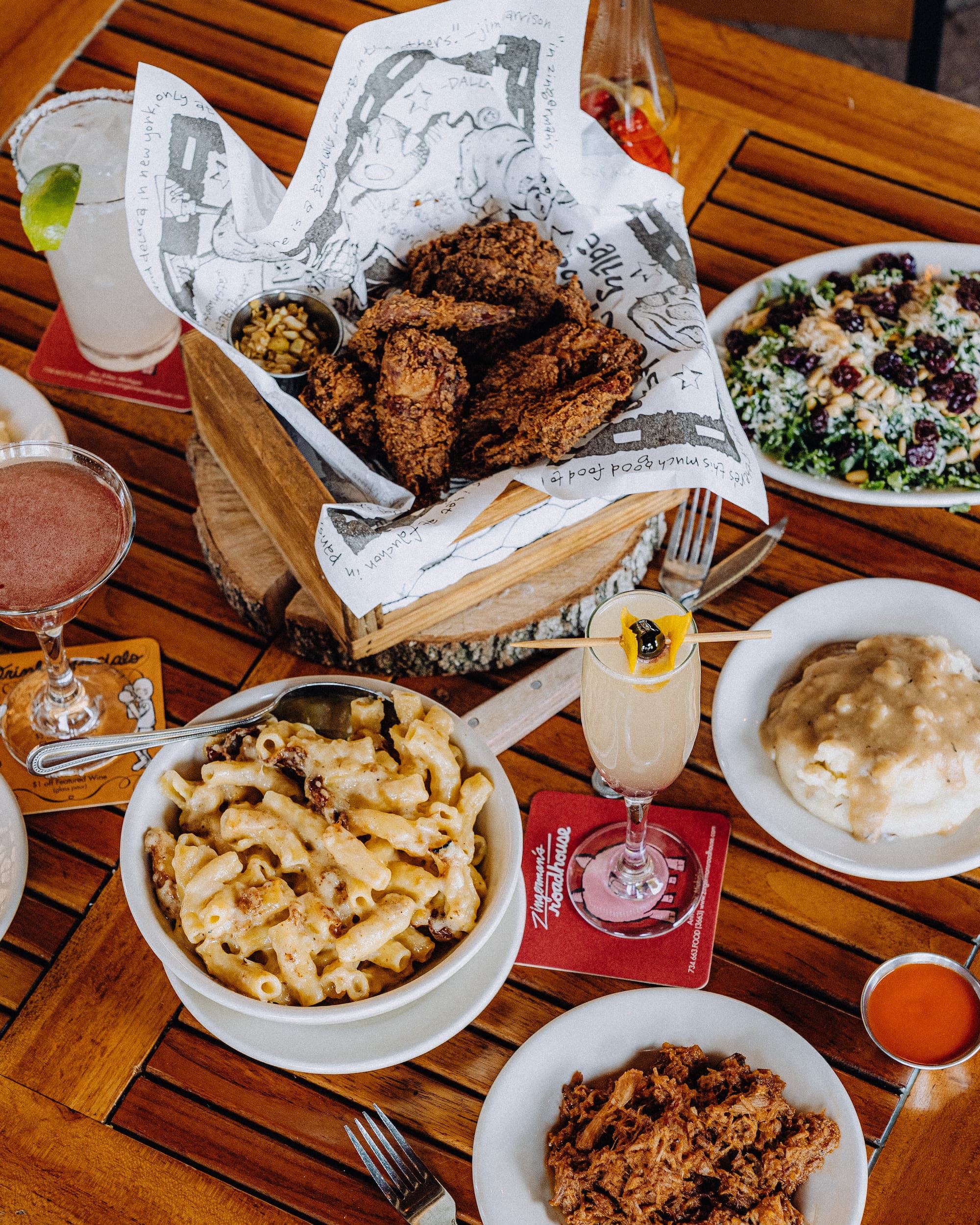 An overhead shot of fried chicken, mac and cheese, pulled pork, biscuits and gravy, and cocktails on a Zingerman's Roadhouse table