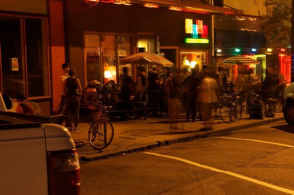 A band playing on the small stage at Flicker Theatre & Bar under string lights, with a full room seated at tables