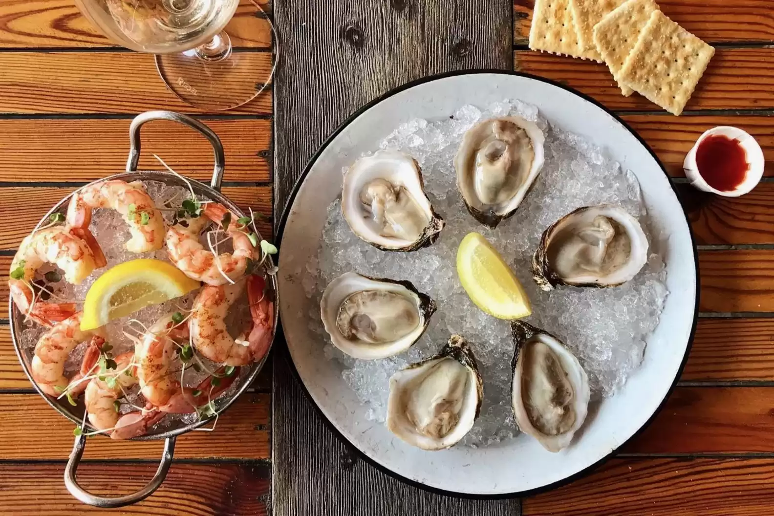 A silver platter of chilled shrimp and a plate of six oysters on ice with lemon wedges, crackers, and cocktail sauce at Seabear Oyster Bar