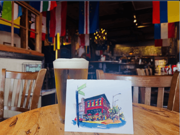 A pint of beer beside an illustrated postcard of The Globe's corner building, international flags hanging overhead
