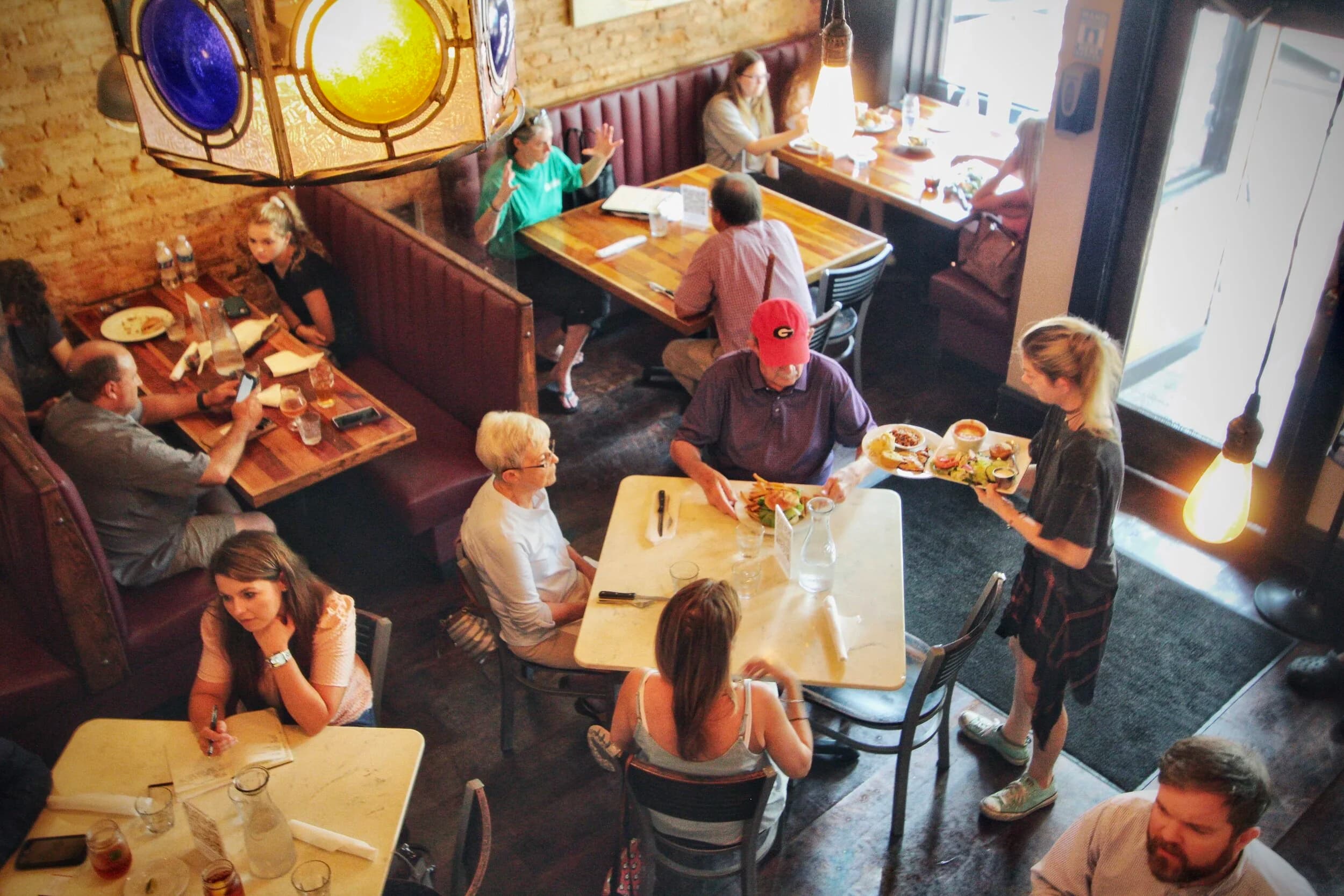 An elevated view of a full dining room at The Place on game day, a server delivering plates to a table