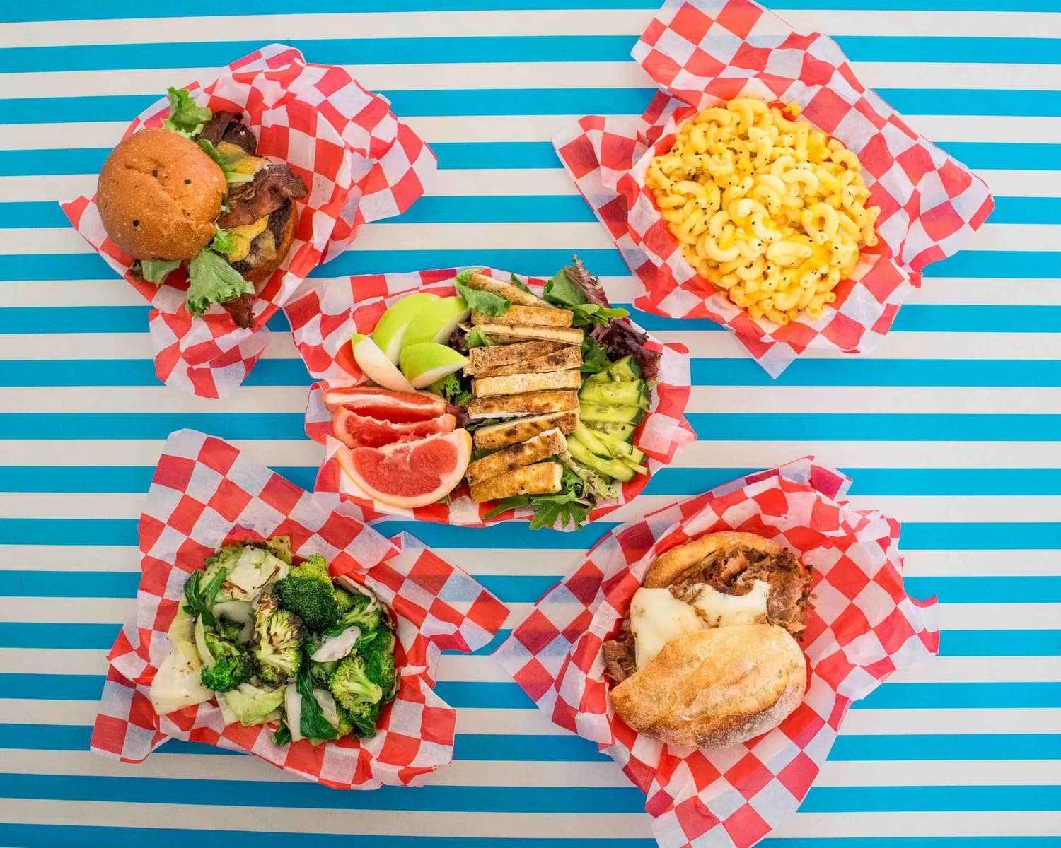Five red-and-white checkered baskets of White Tiger Gourmet food, including a burger, mac and cheese, and a pulled pork sandwich