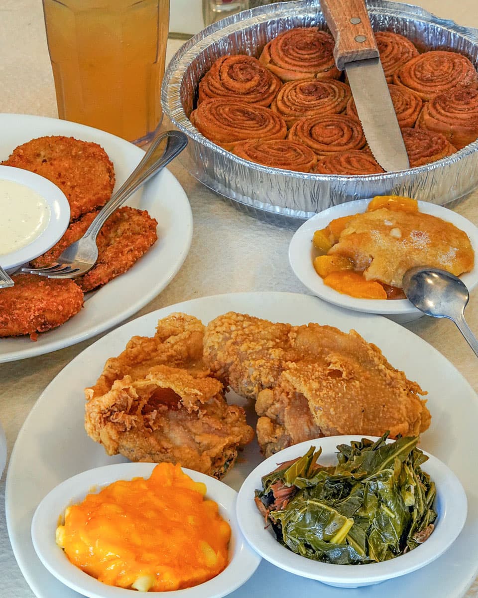 Fried chicken, fried green tomatoes, mac and cheese, collard greens, peach cobbler, and cinnamon rolls spread across a table at Mary Mac's Tea Room