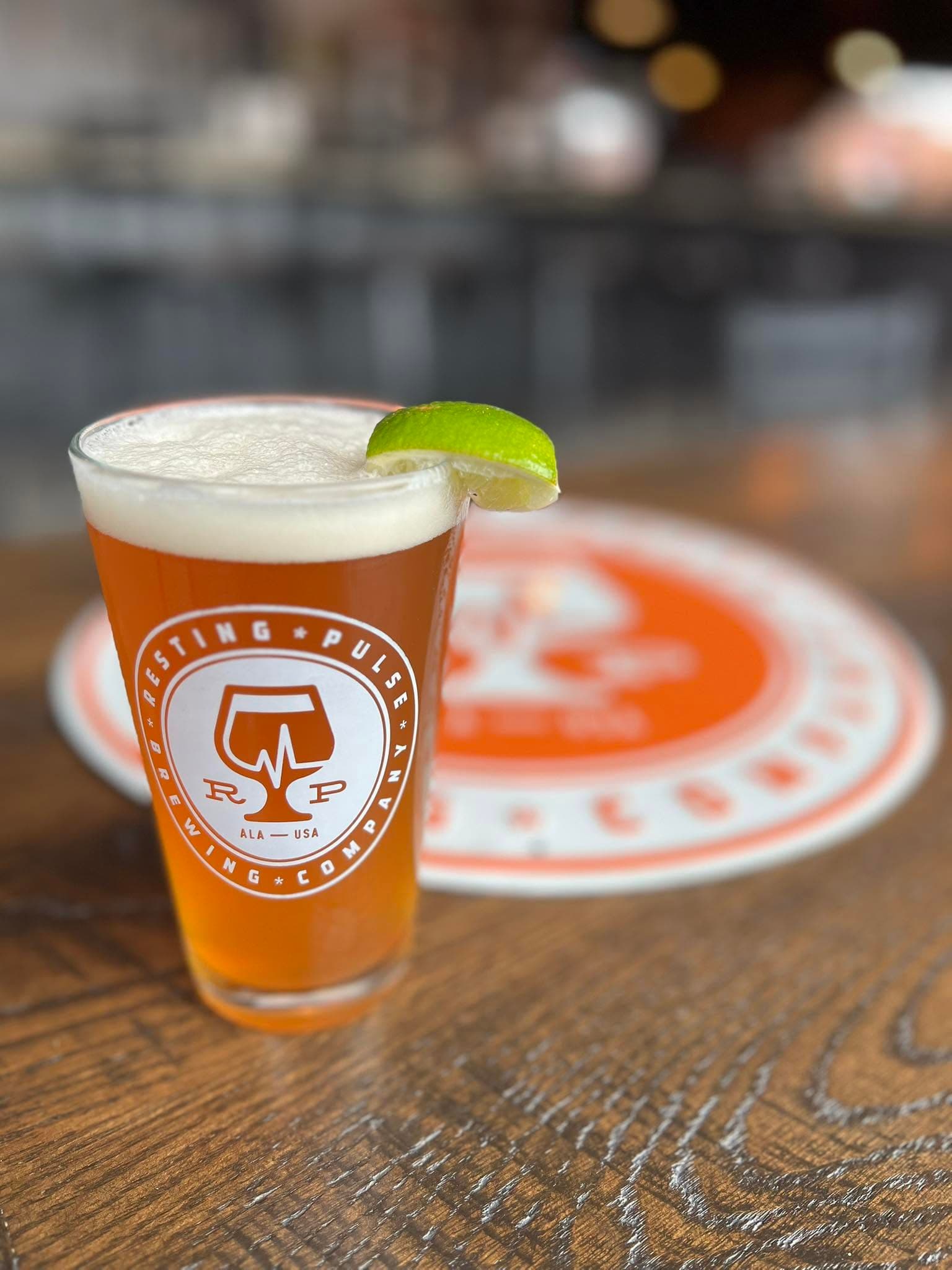 A lime-garnished beer in a branded Resting Pulse Brewing Company pint glass on the taproom bar