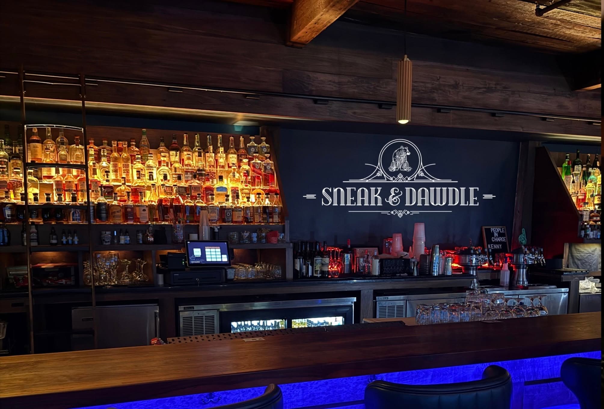 Sneak & Dawdle's back-lit bottle wall and neon bear logo behind a long wooden bar