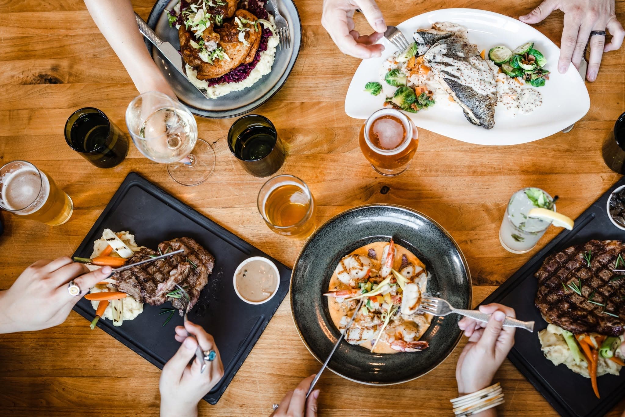 An overhead shot of a shared table at The Depot with steaks, seared fish, shrimp, wine, and beer
