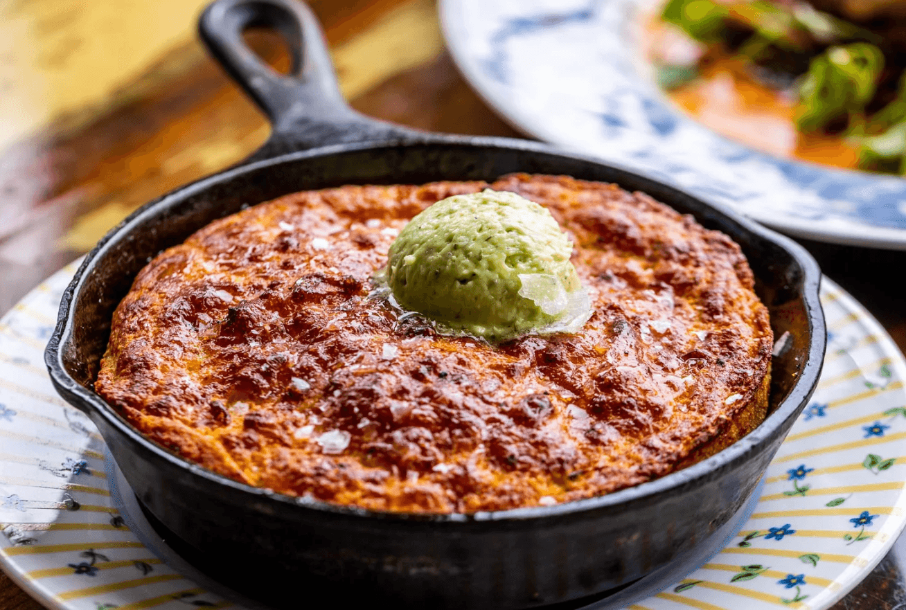 Odd Duck's cast-iron cornbread topped with a scoop of herb butter and flaky salt, plated on a striped dish