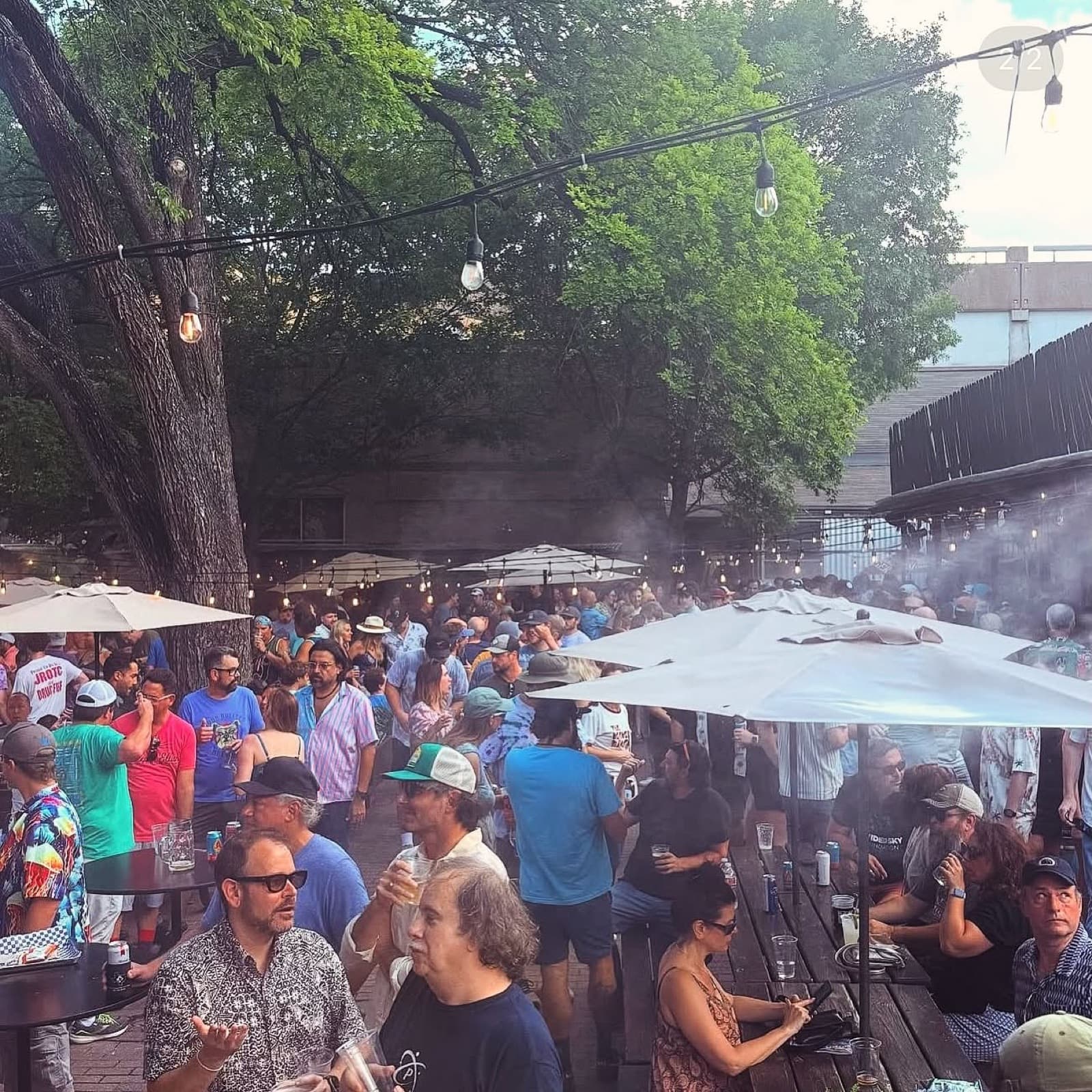 A packed shaded beer garden at Scholz Garten under string lights and umbrellas