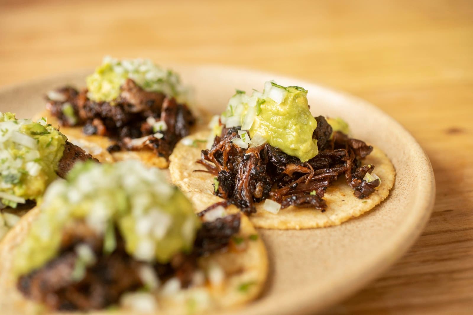 Birria tacos topped with diced onion and guacamole on a plate at Suerte