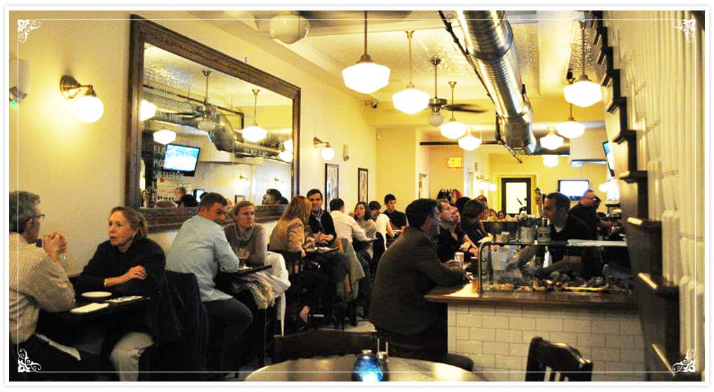 The upstairs dining room at Thames Street Oyster House, framed prints on cream walls above a mirrored bar with a raw bar setup