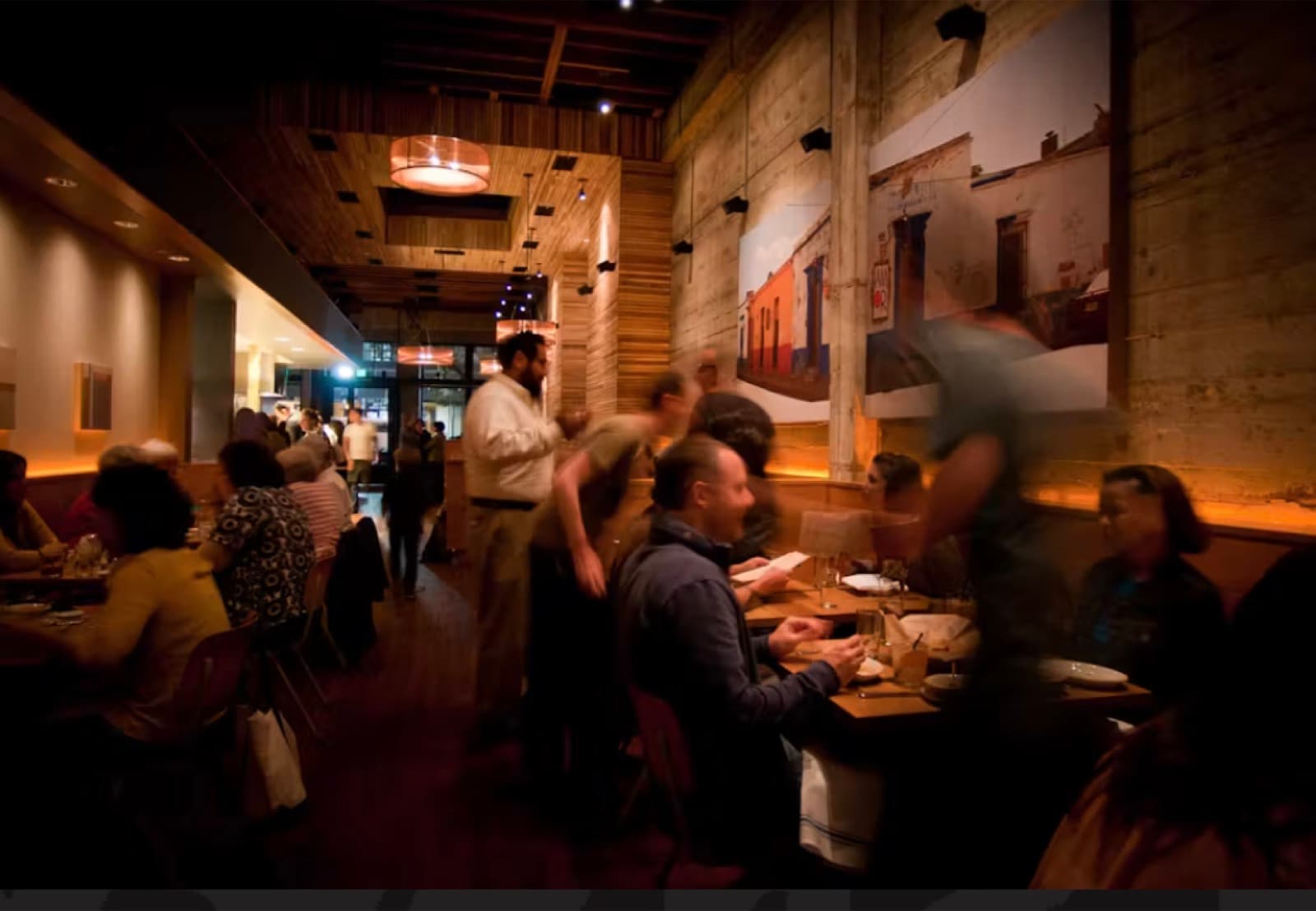 Comal's dining room at dusk with staff moving between wood-lined booths and a lit bar