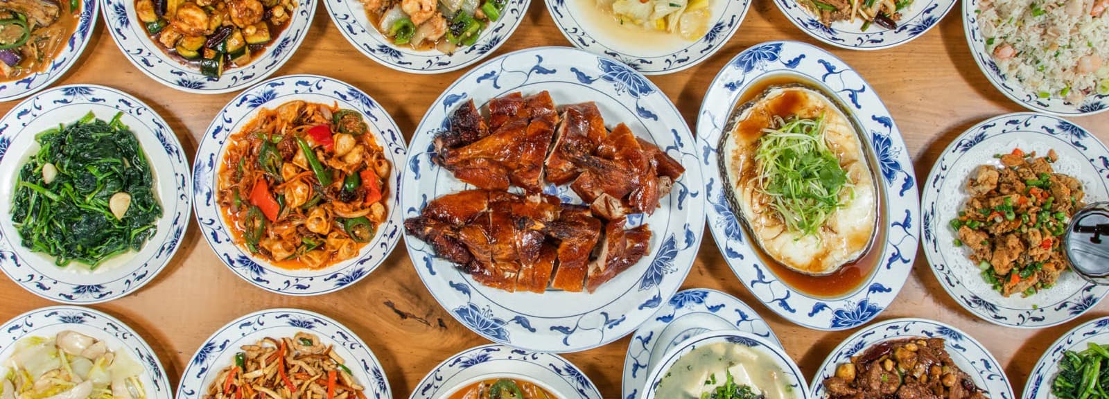 A spread of Great China dishes on blue-and-white plates, including roasted meats, greens, and fried rice