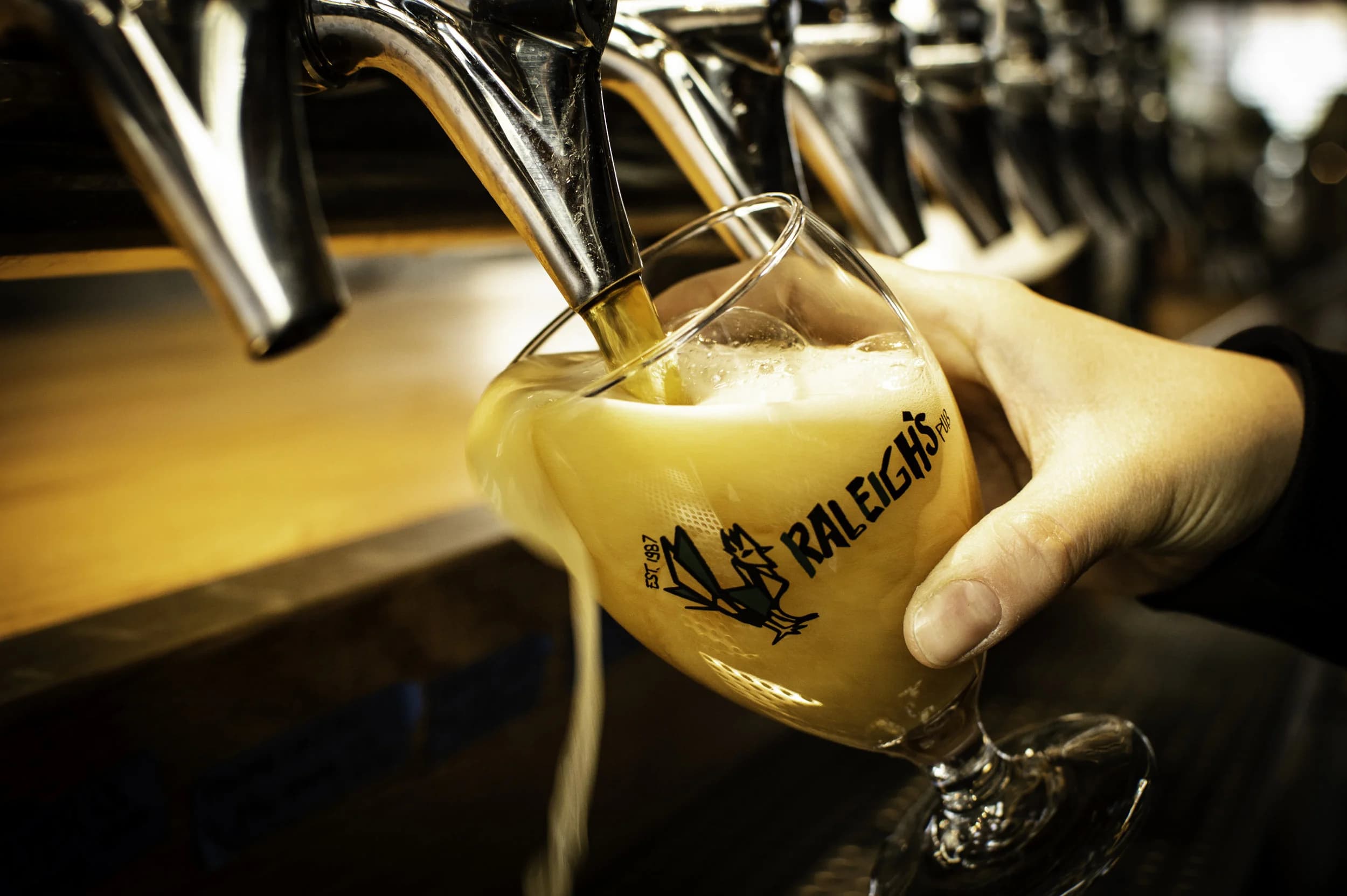 A branded Raleigh's Pub goblet glass being filled with beer straight from the tap