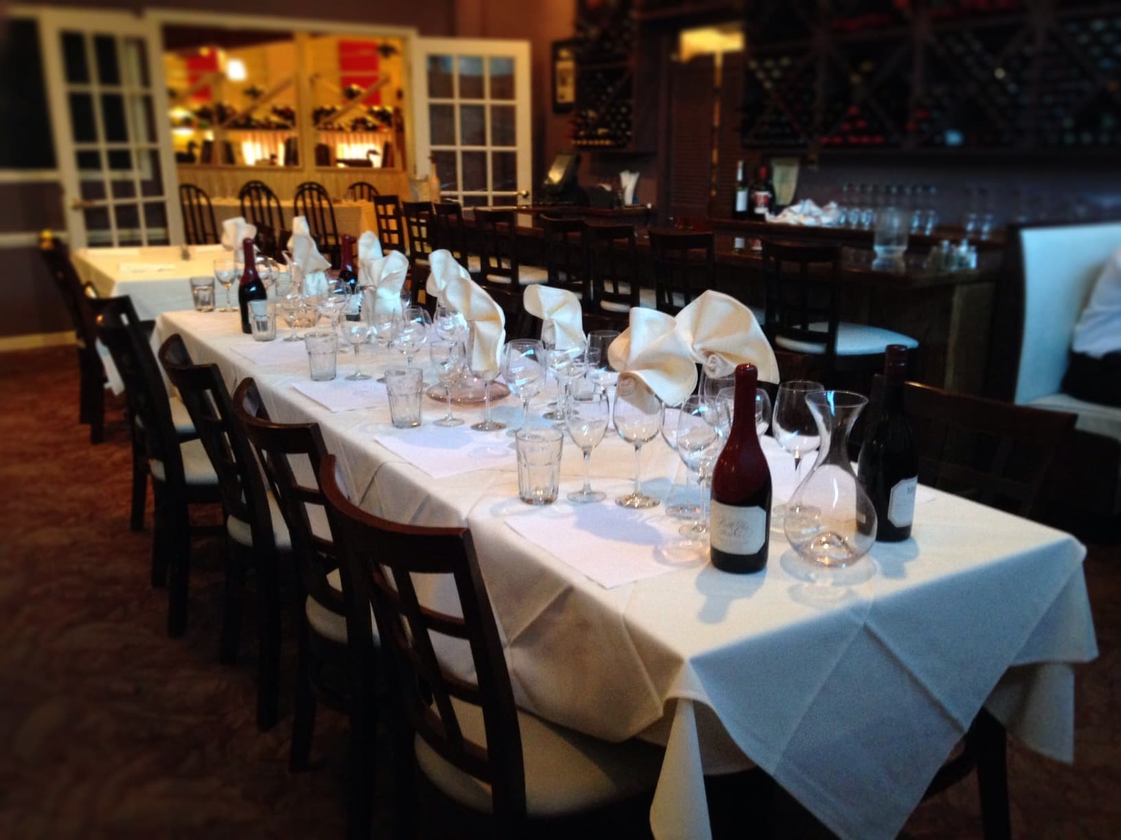 A long white-clothed private dining table set with wine glasses and bottles at 622 North, with the wine cellar wall behind