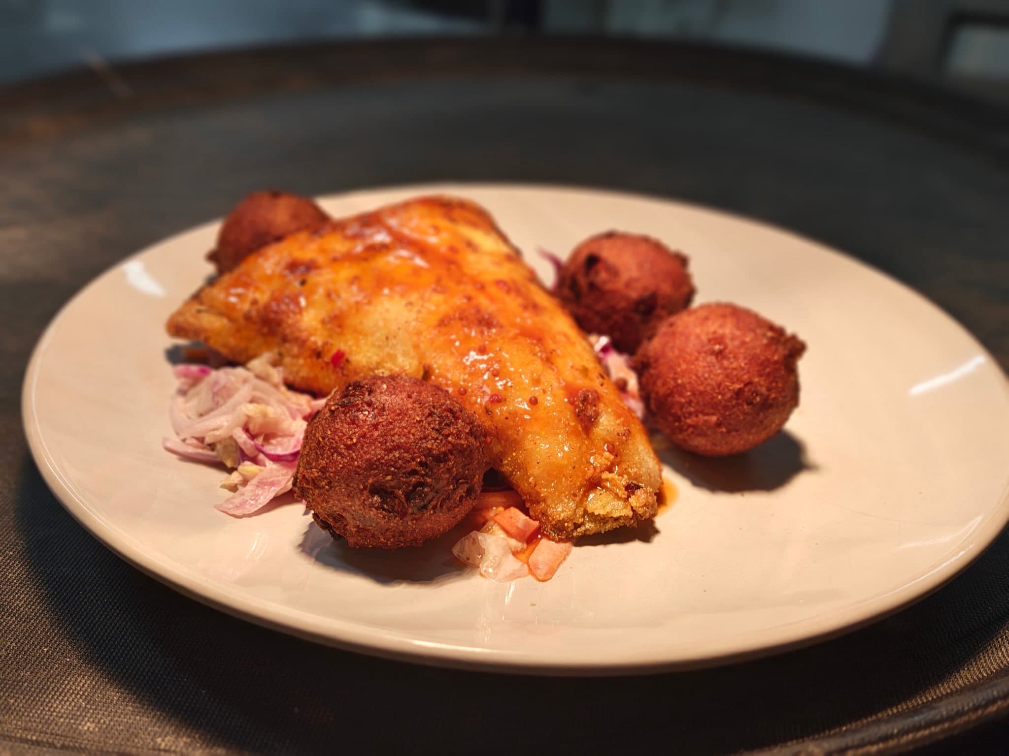 A glazed fried fish fillet with hush puppies and red onion slaw on a plate at The Maroon Door
