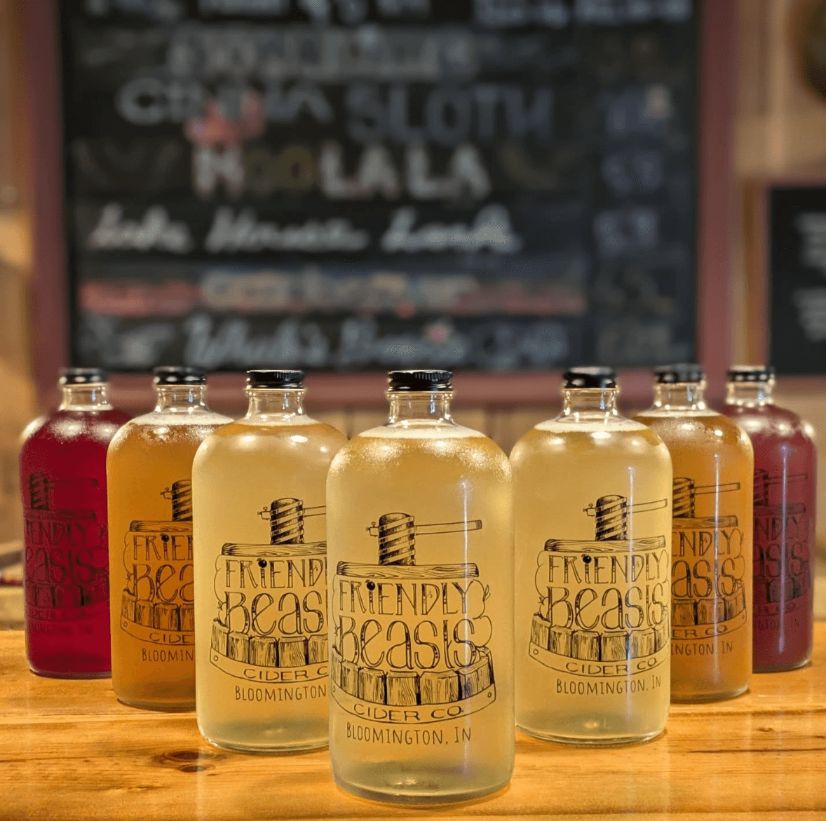 A row of branded Friendly Beasts Cider Co. bottles filled with different-colored ciders on the tasting-room bar