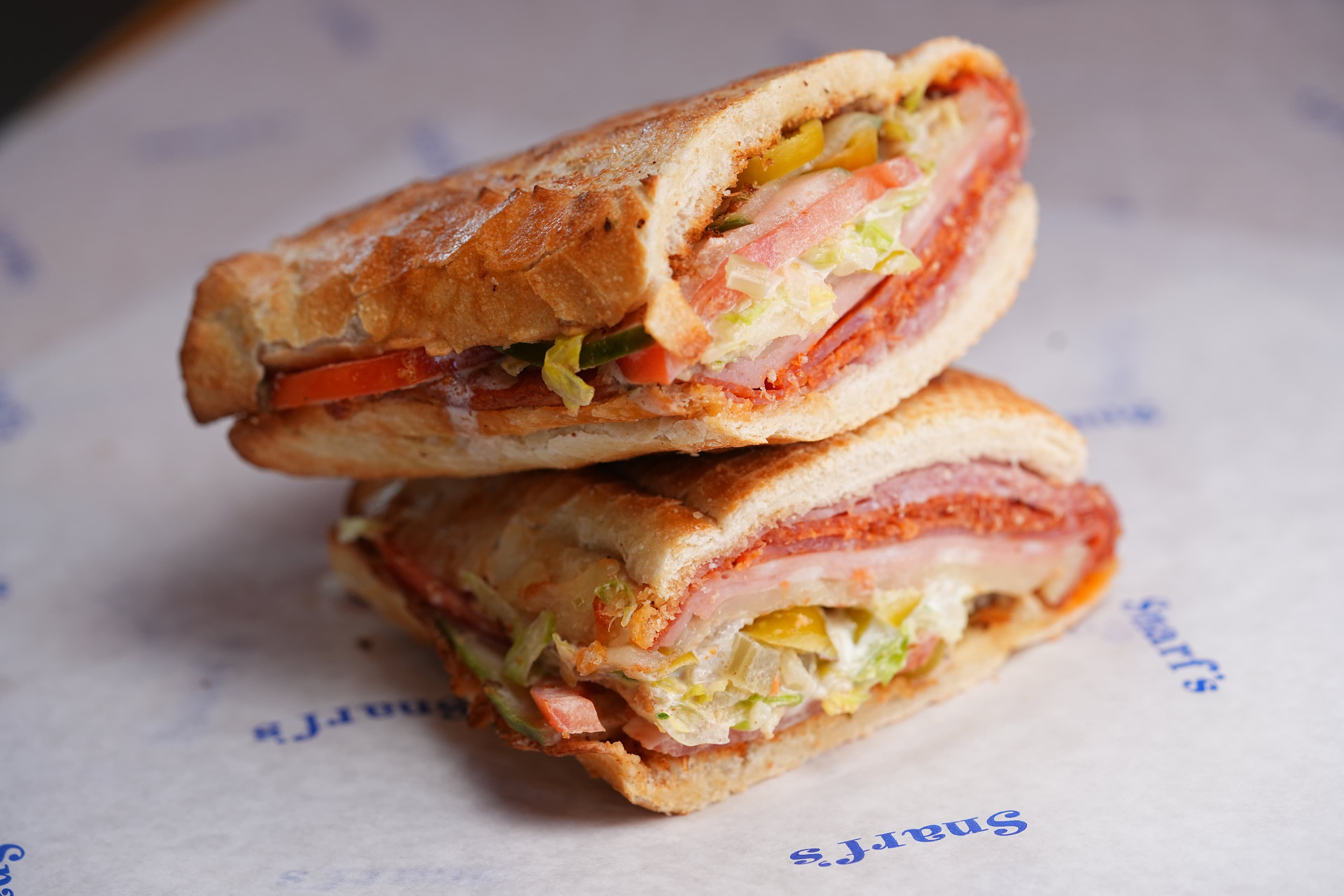 Two toasted Snarf's sandwich halves stacked, stuffed with meats, cheese, and shredded lettuce, on Snarf's-branded paper