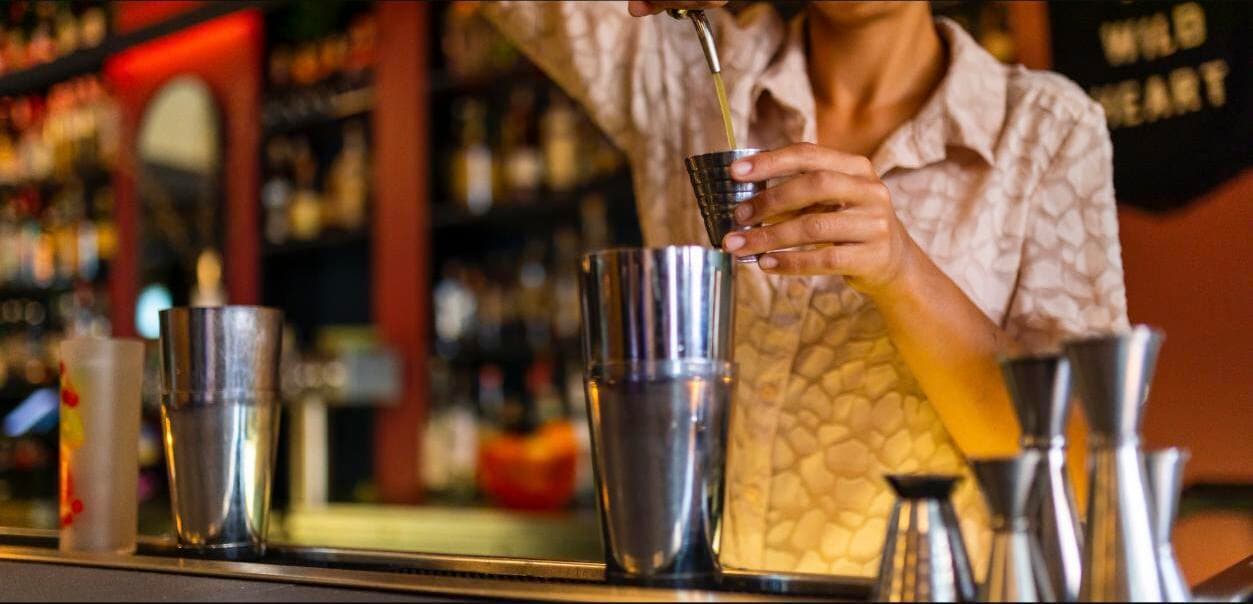 A bartender at Marble + Rye pouring a fresh-mixed cocktail from a shaker into a glass