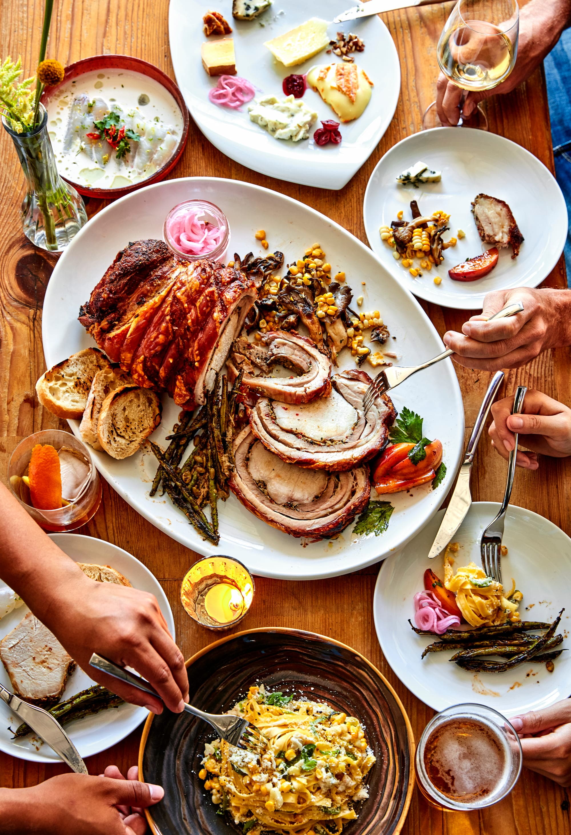 A shared table at The Dapper Goose with a whole roasted porchetta, pasta, salads, and cocktails
