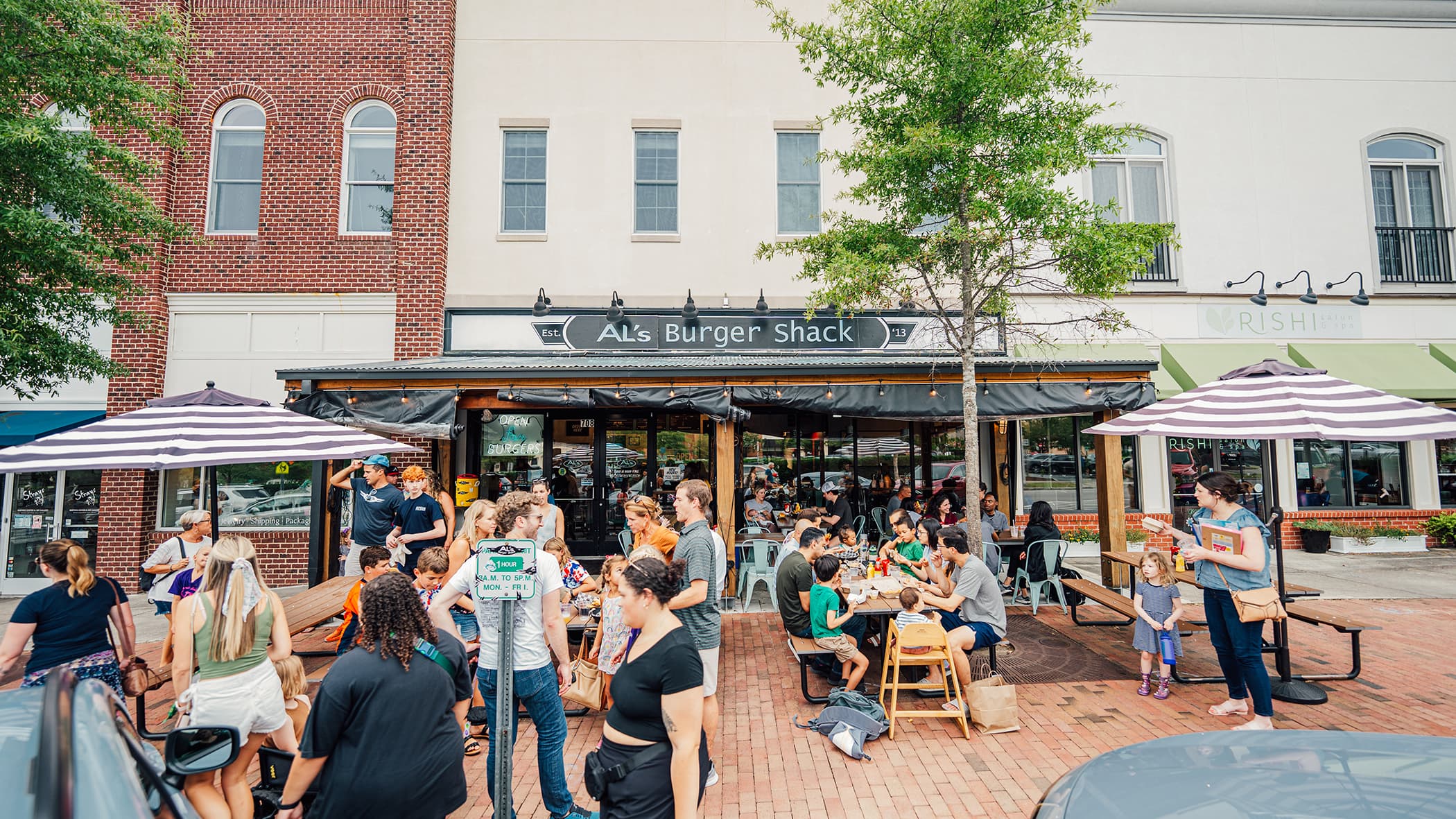The Al's Burger Shack storefront with a busy patio of diners under striped umbrellas on a downtown sidewalk