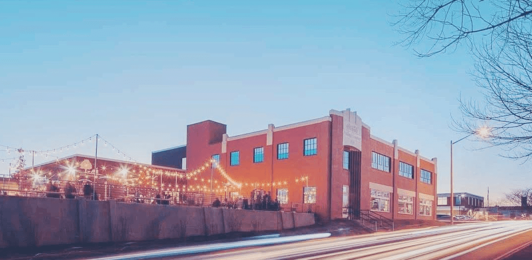Kardinal Hall's brick beer-hall building strung with string lights at dusk, its patio glowing beside the road