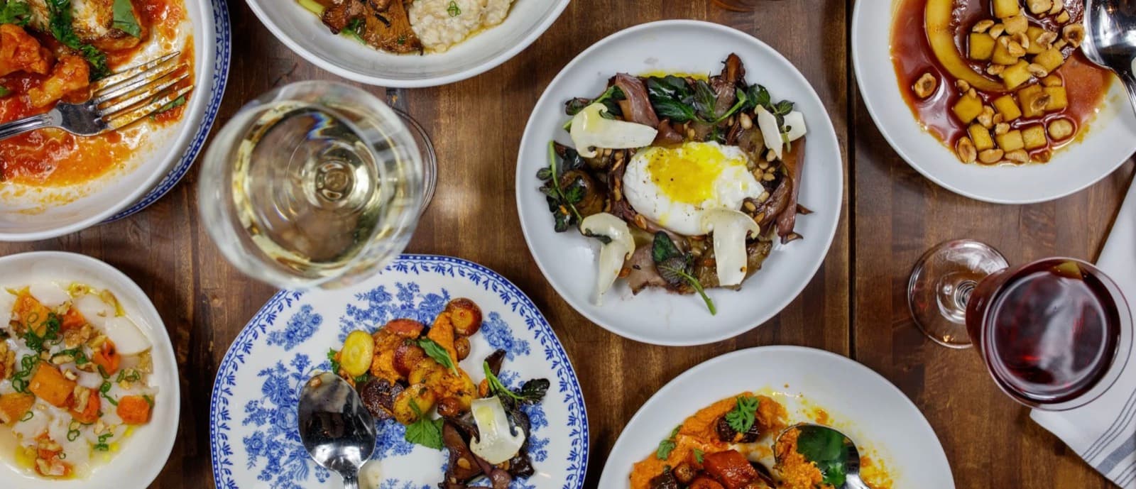 An overhead shot of a shared table at Thistle & Leek with small plates, a poached egg dish, and glasses of wine