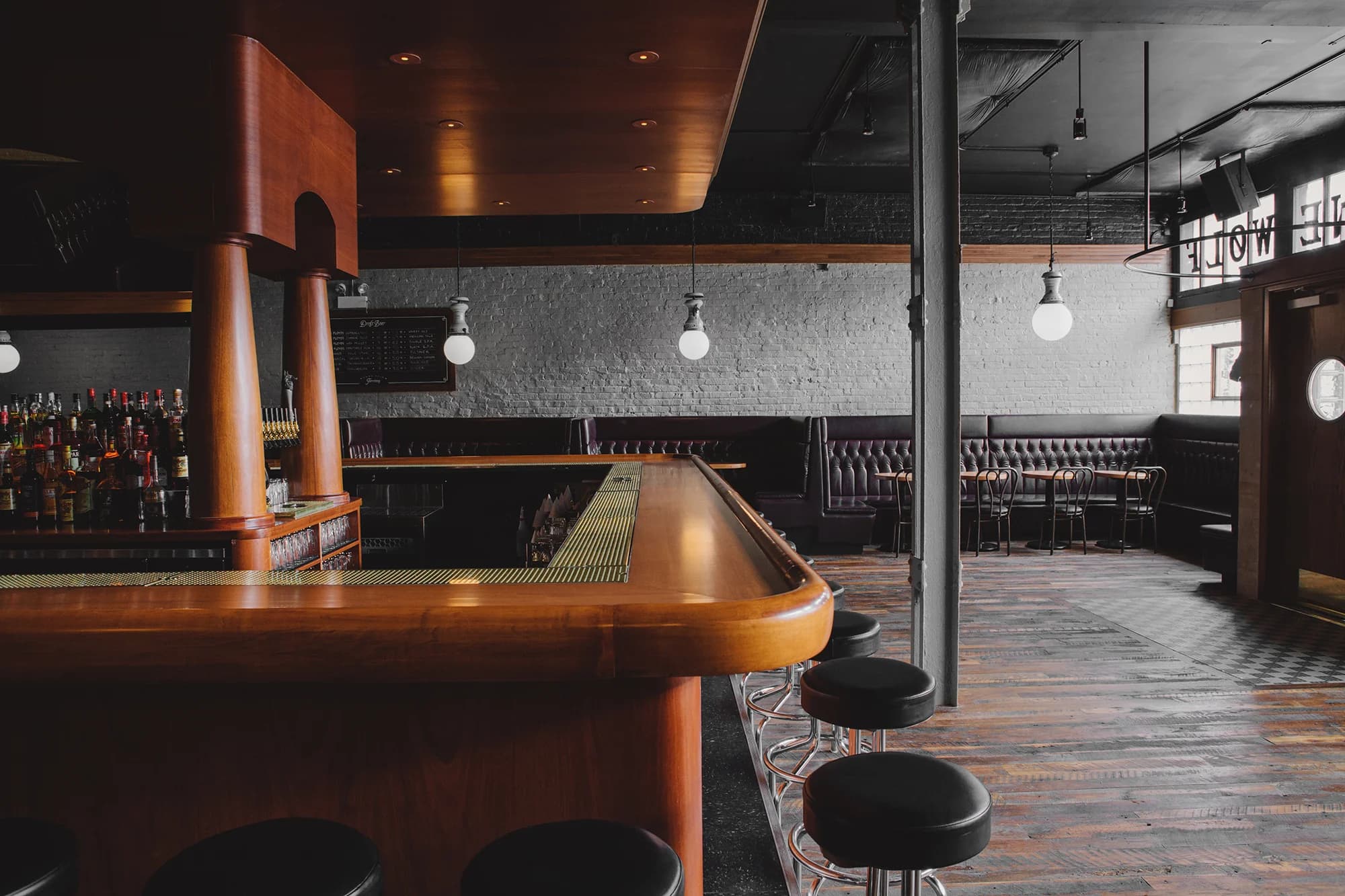 Lone Wolf Tavern's wood-topped bar and leather booths under the illuminated wolf sign by the entrance