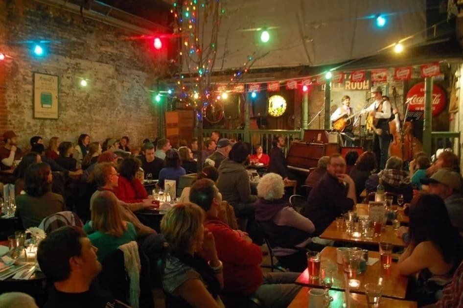 A band playing on a small stage under string lights at Arnold's Bar and Grill, with a full crowd seated at tables