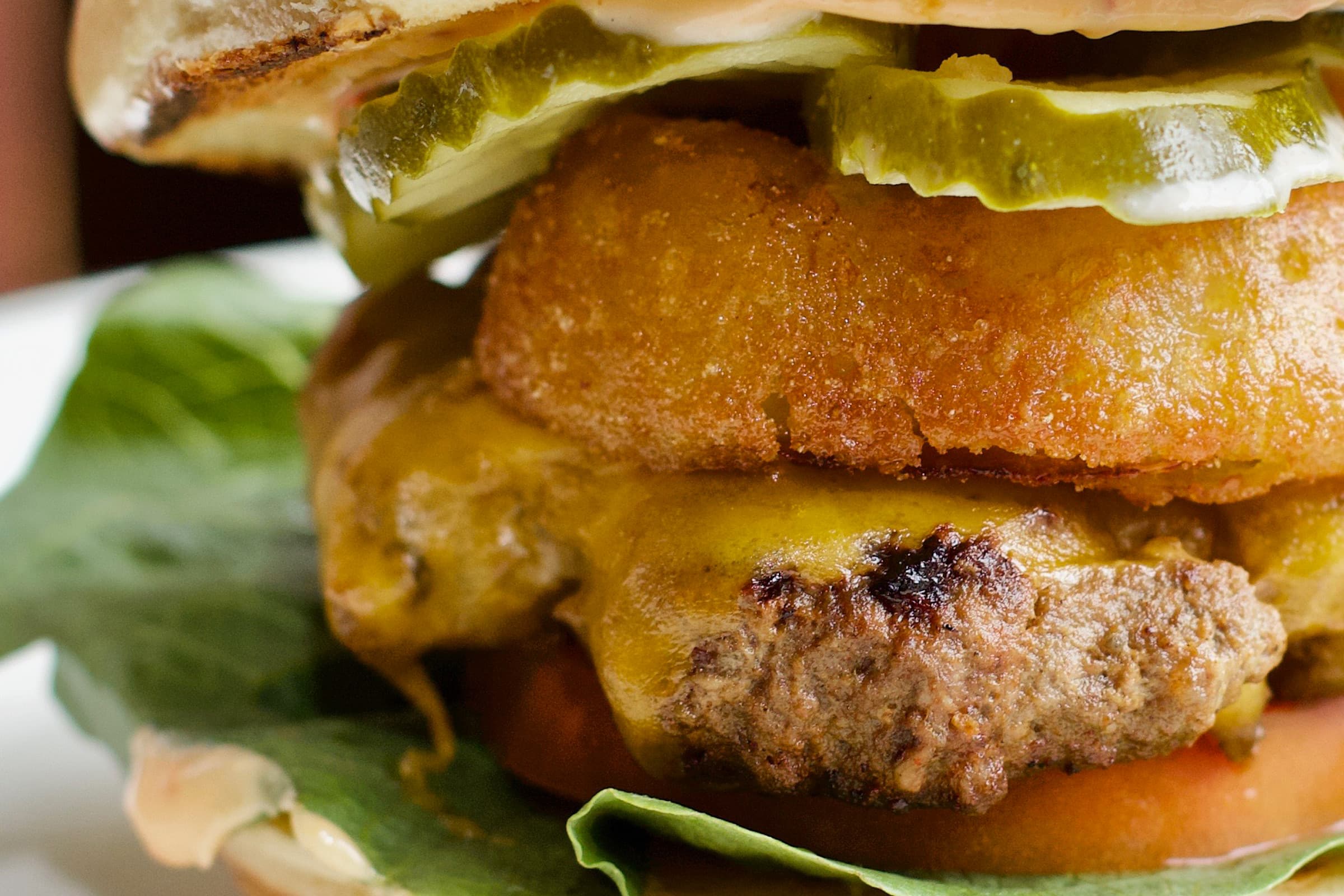 A close-up of a stacked cheeseburger with a fried green ring, pickles, and lettuce at MOTR Pub