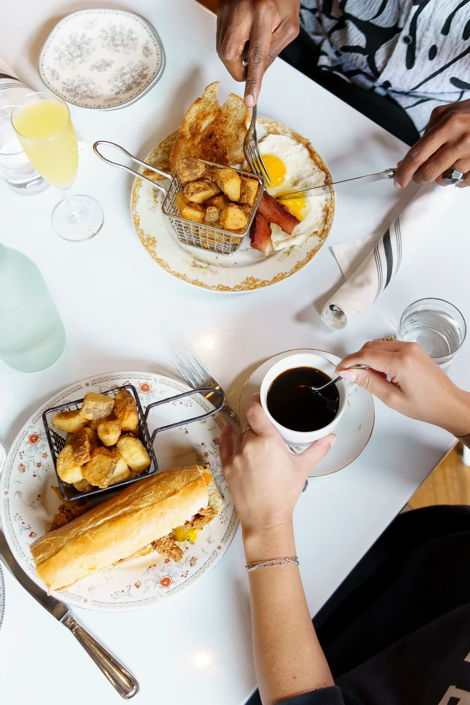 Overhead shot of a Pennyroyal Station brunch table — eggs, bacon, fried potatoes, a toasted baguette sandwich, mimosa, and coffee