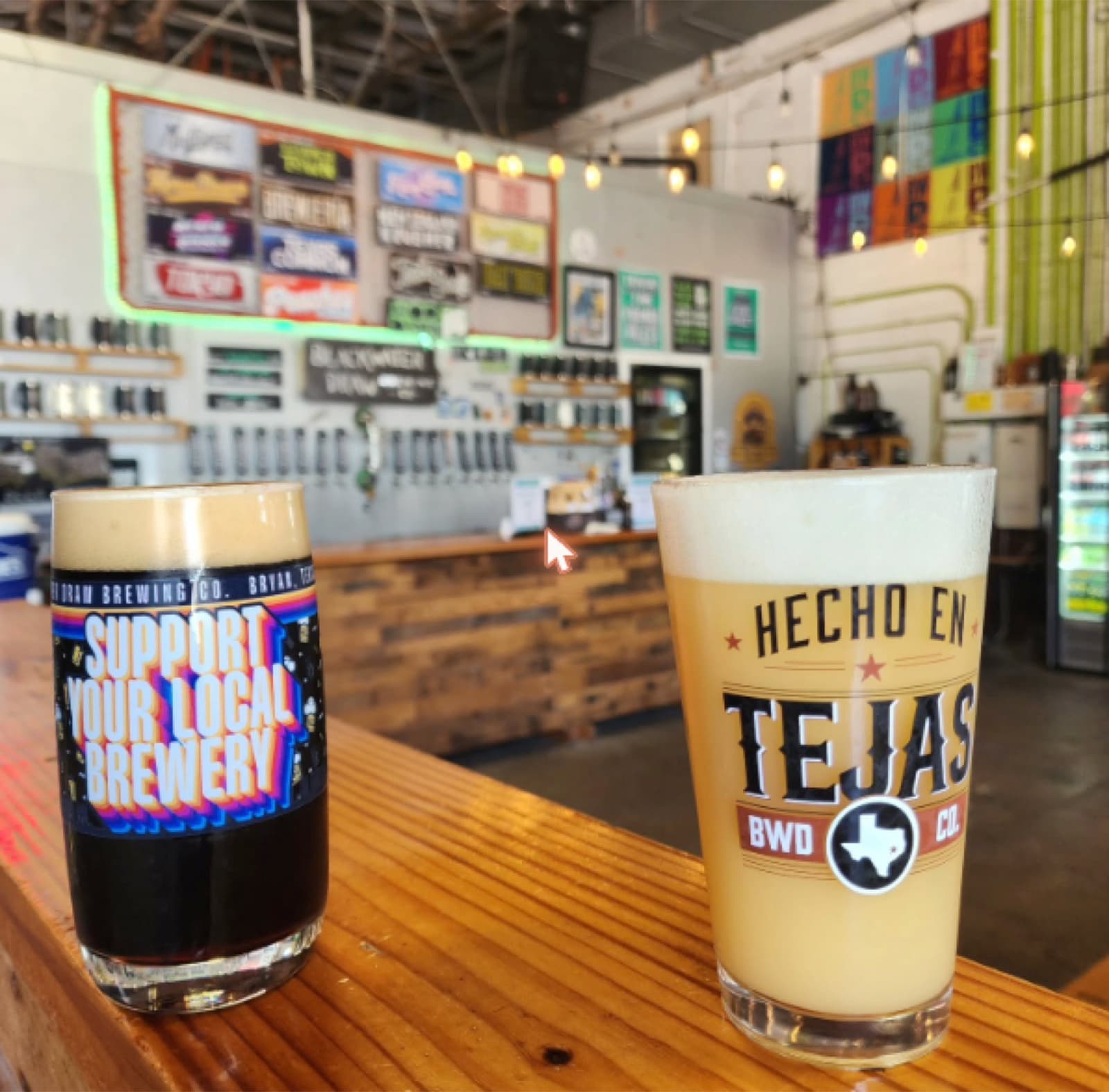 Two pint glasses of beer on the bar at Blackwater Draw Brewing Co, taps and neon beer signs behind
