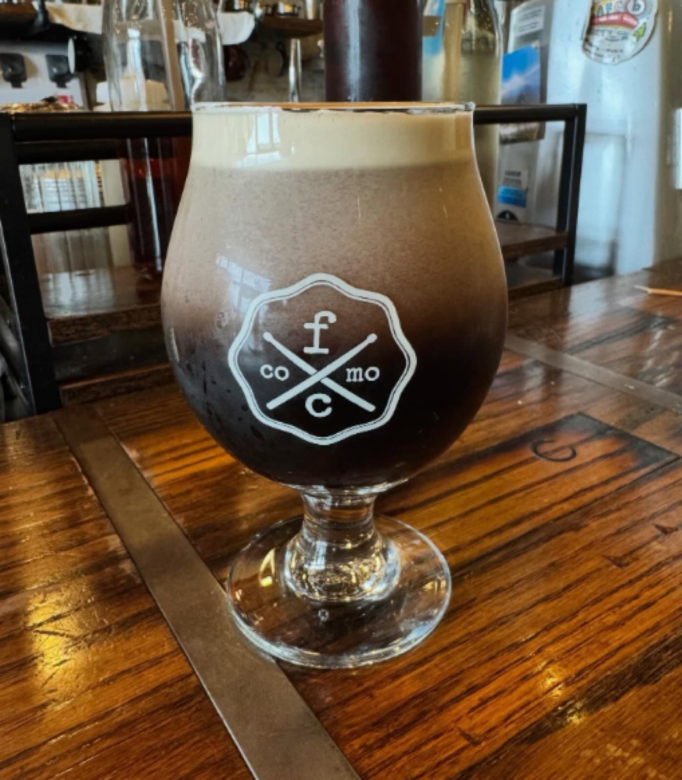 A dark stout in a branded Fretboard Coffee 'CoMo' snifter glass on a wood table