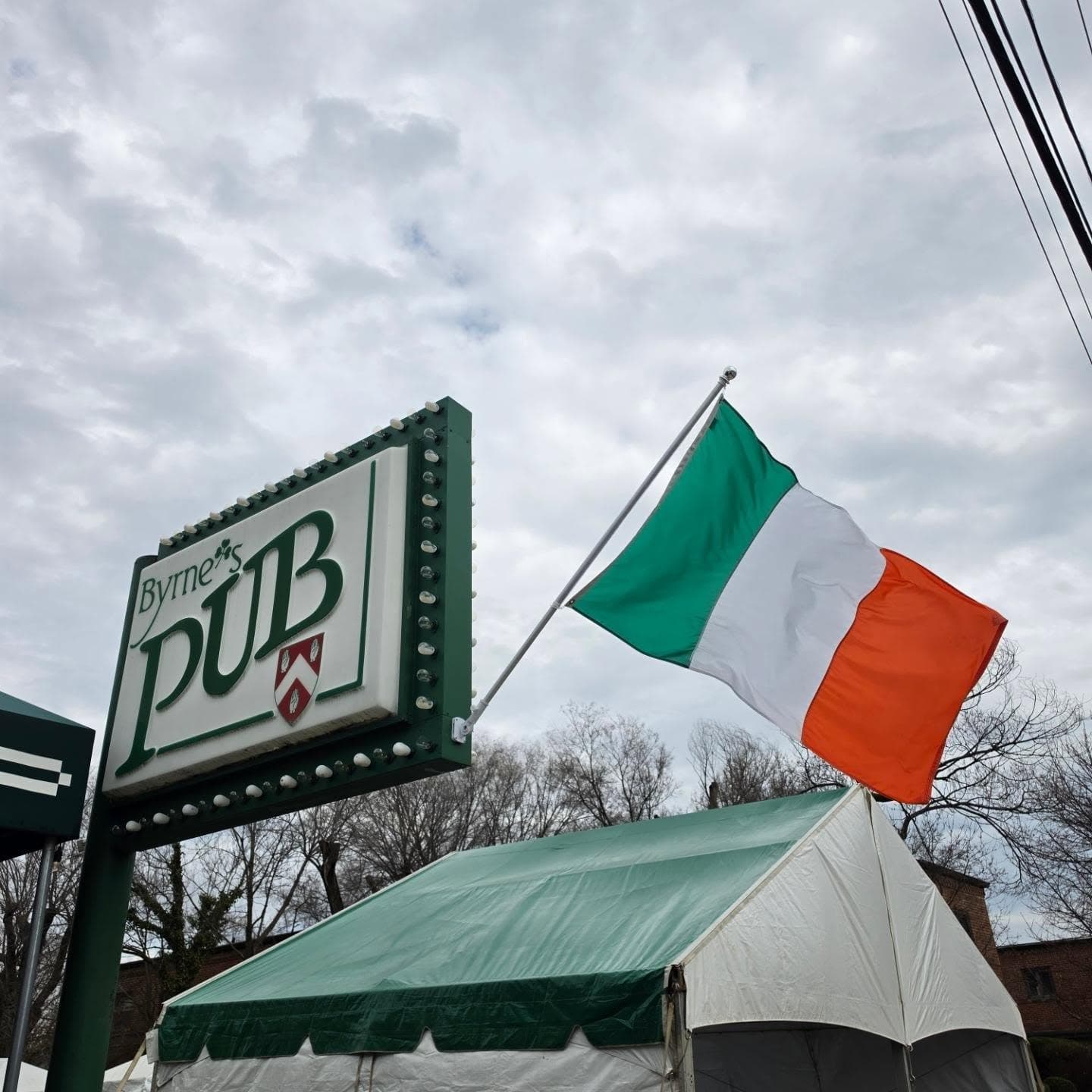 Byrne's Pub's lit sign with an Irish flag flying above the entrance tent