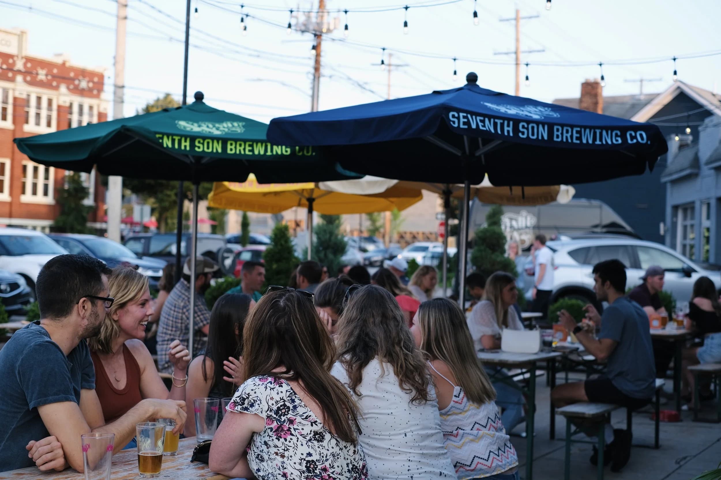 A crowd on Seventh Son Brewing Co.'s patio under string lights and umbrellas branded with the brewery's name