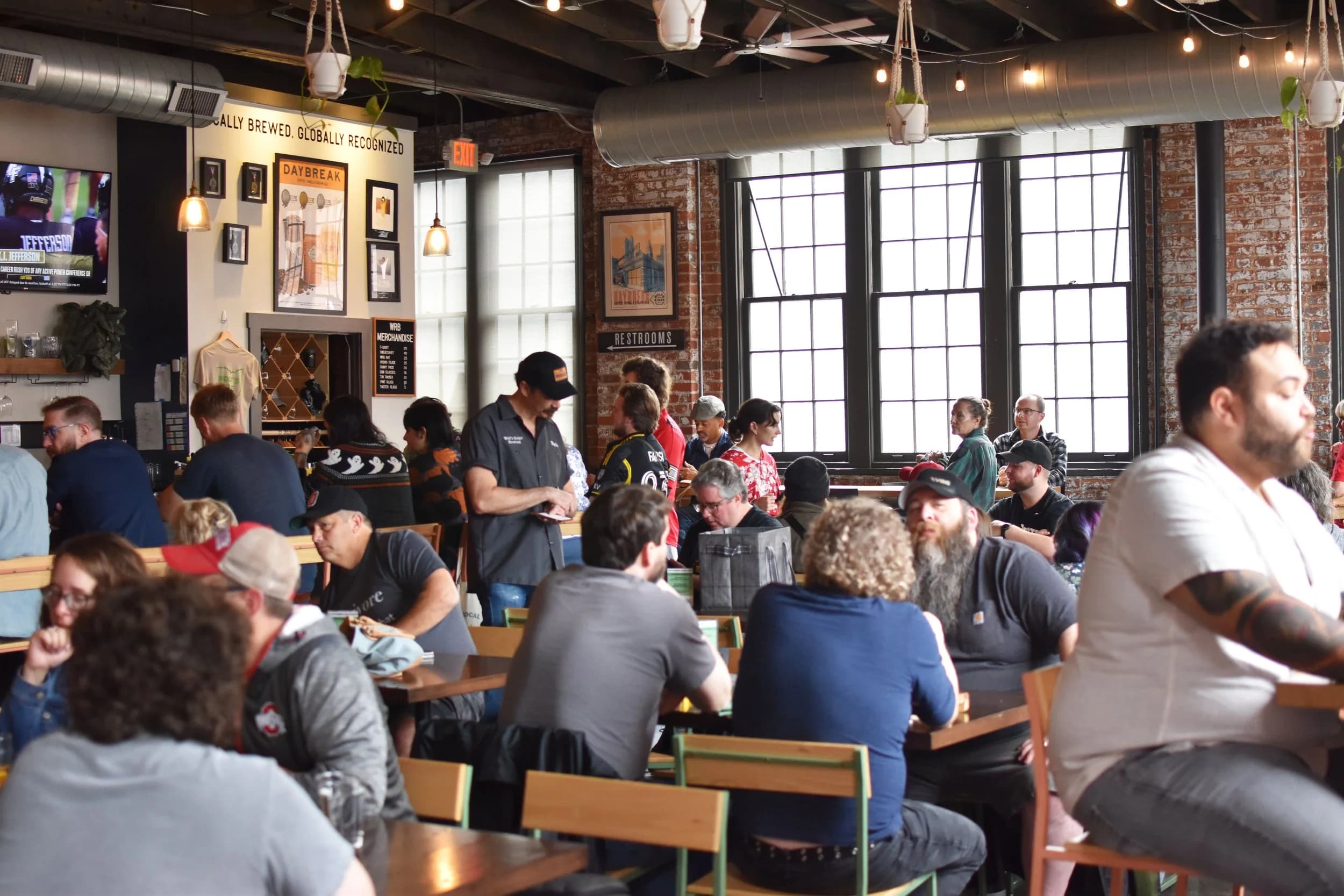 A packed dining room under Wolf's Ridge Brewing's exposed brick and metal ceiling, with the Daybreak beer poster on the wall