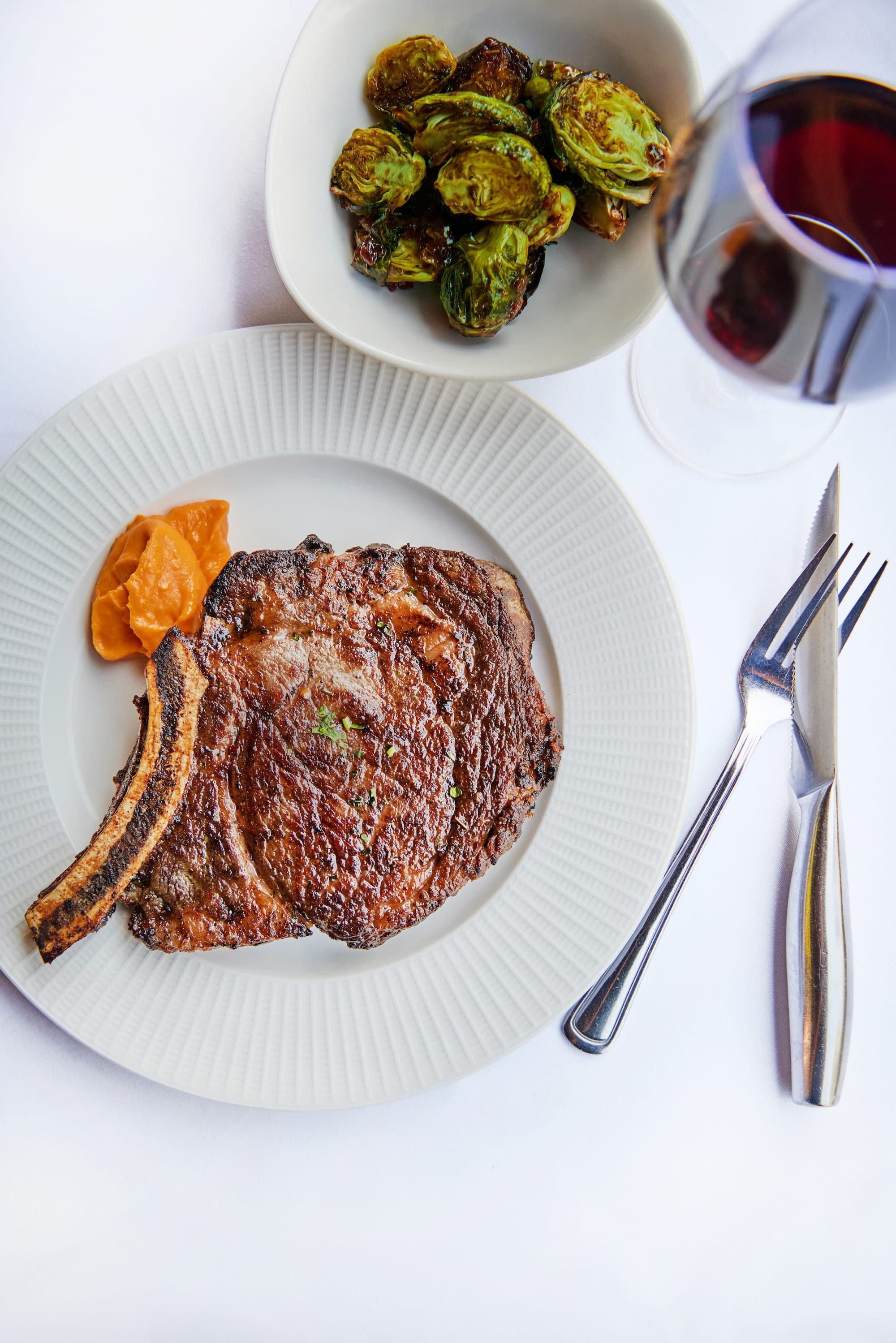 A grilled ribeye with Brussels sprouts on a plate beside a bowl of macaroni and cheese and a martini at Al Biernat's
