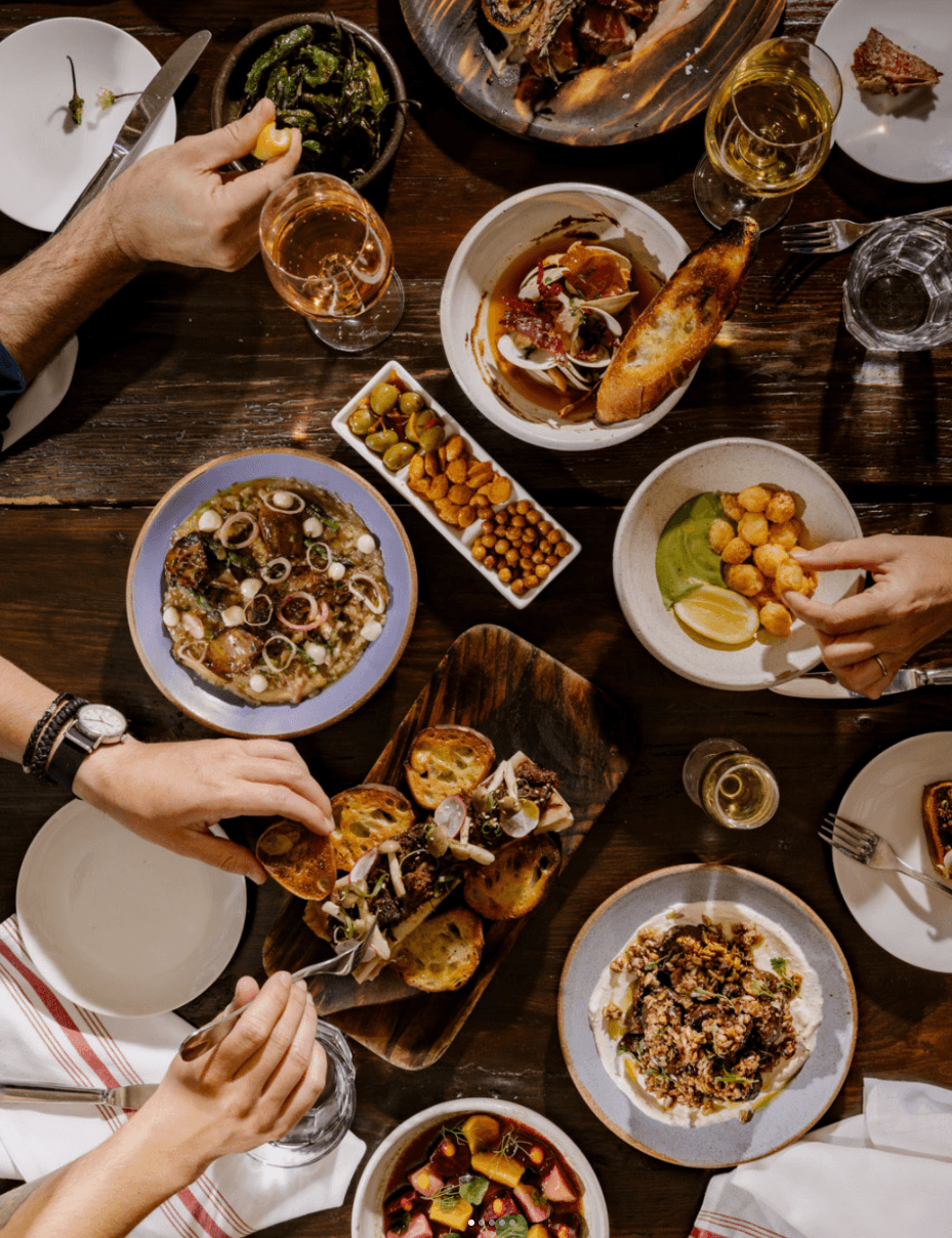 A table crowded with tapas plates at Mateo Bar de Tapas — croquetas, mussels, a lamb flatbread, olives, and glasses of wine