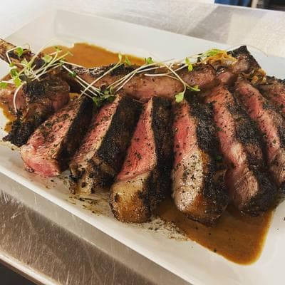 A sliced ribeye with a peppercorn crust and microgreens, drizzled in sauce on a white plate at NanaSteak