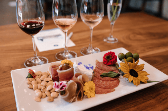 A wine flight beside a charcuterie board of cured meats, cheese, olives and flowers at J. Scott Cellars