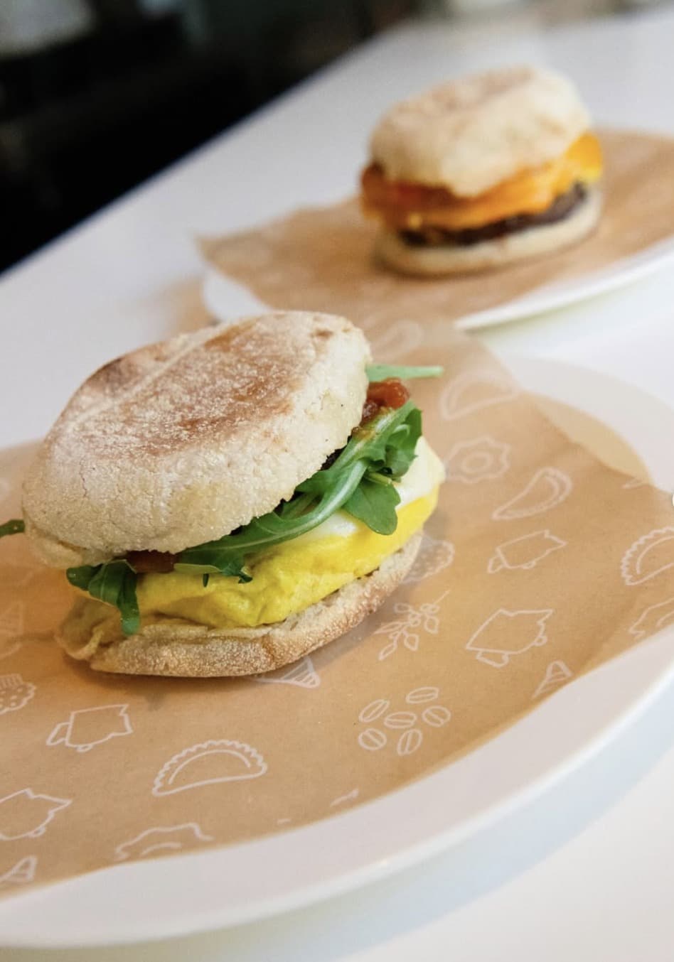 Two breakfast sandwiches on English muffins — egg, arugula, and cheese — on parchment paper at Brothers K Coffeehouse